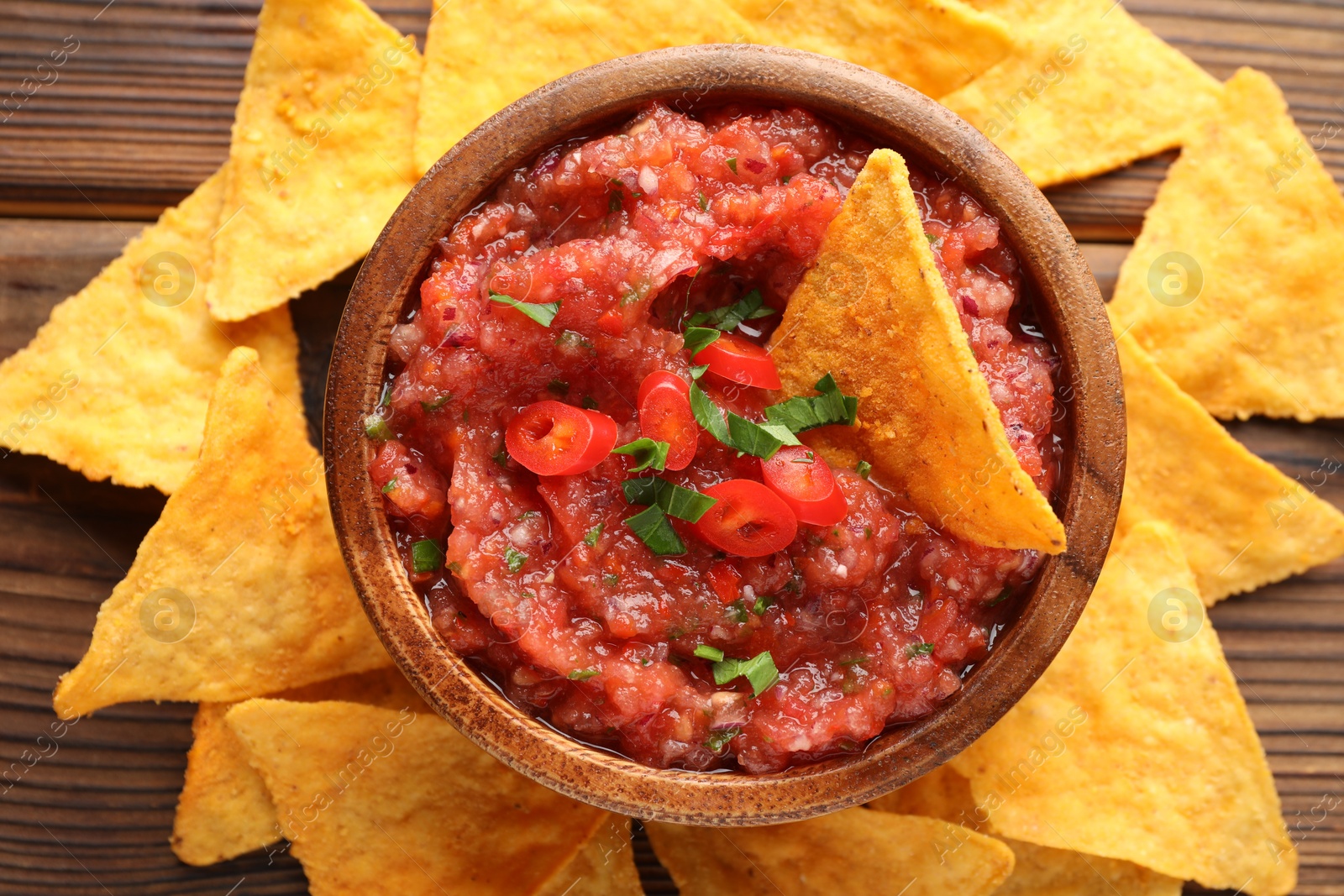 Photo of Delicious spicy salsa sauce in bowl and nacho chips on wooden table, flat lay