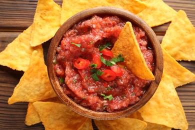 Delicious spicy salsa sauce in bowl and nacho chips on wooden table, flat lay