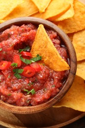 Photo of Delicious spicy salsa sauce in bowl and nacho chips on table, above view