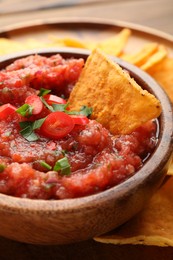 Photo of Delicious spicy salsa sauce with nacho chip in bowl on table, closeup