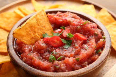 Delicious spicy salsa sauce with nacho chip in bowl on table, closeup