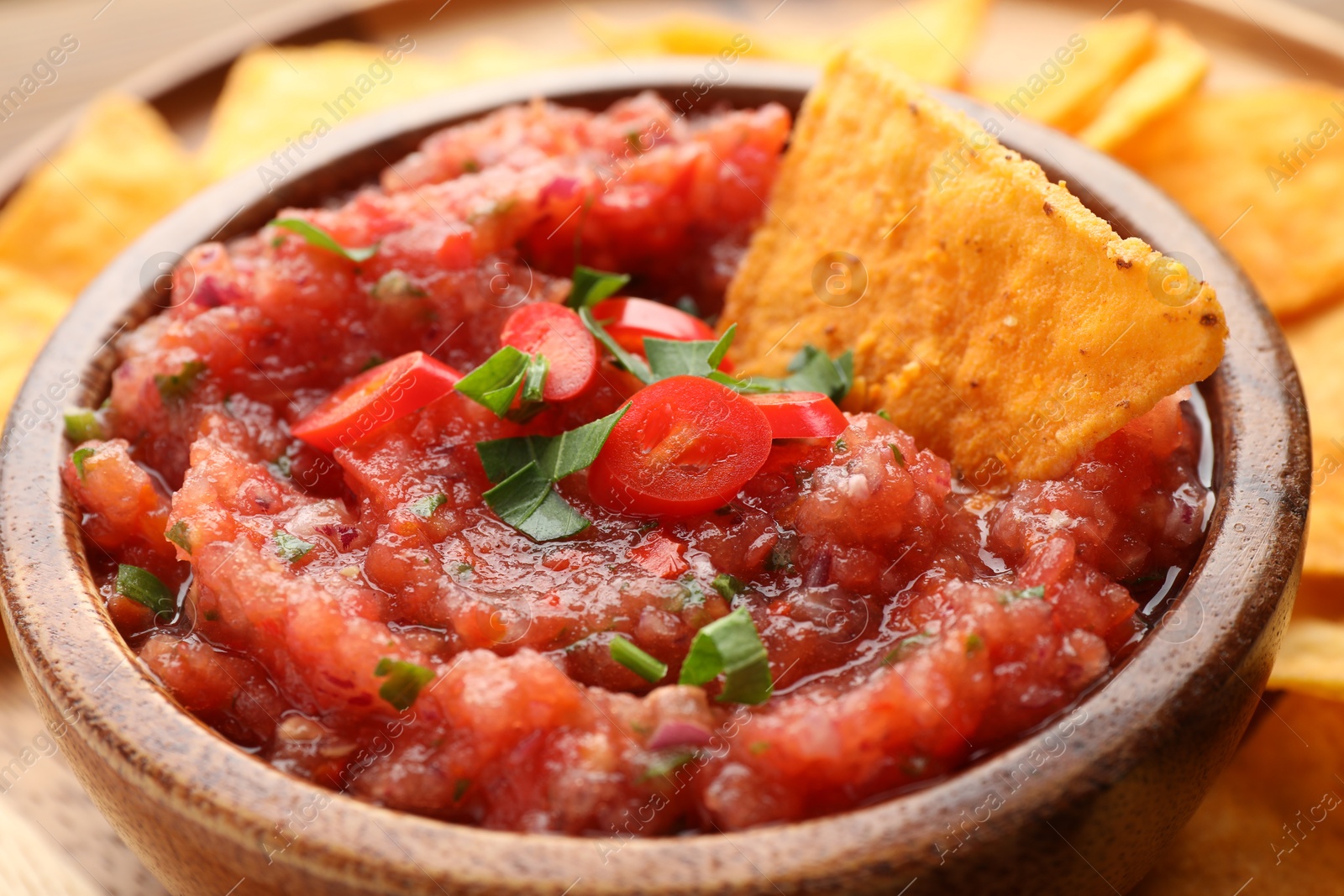 Photo of Delicious spicy salsa sauce with nacho chip in bowl on table, closeup