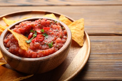 Delicious spicy salsa sauce in bowl and nacho chips on wooden table, closeup. Space for text