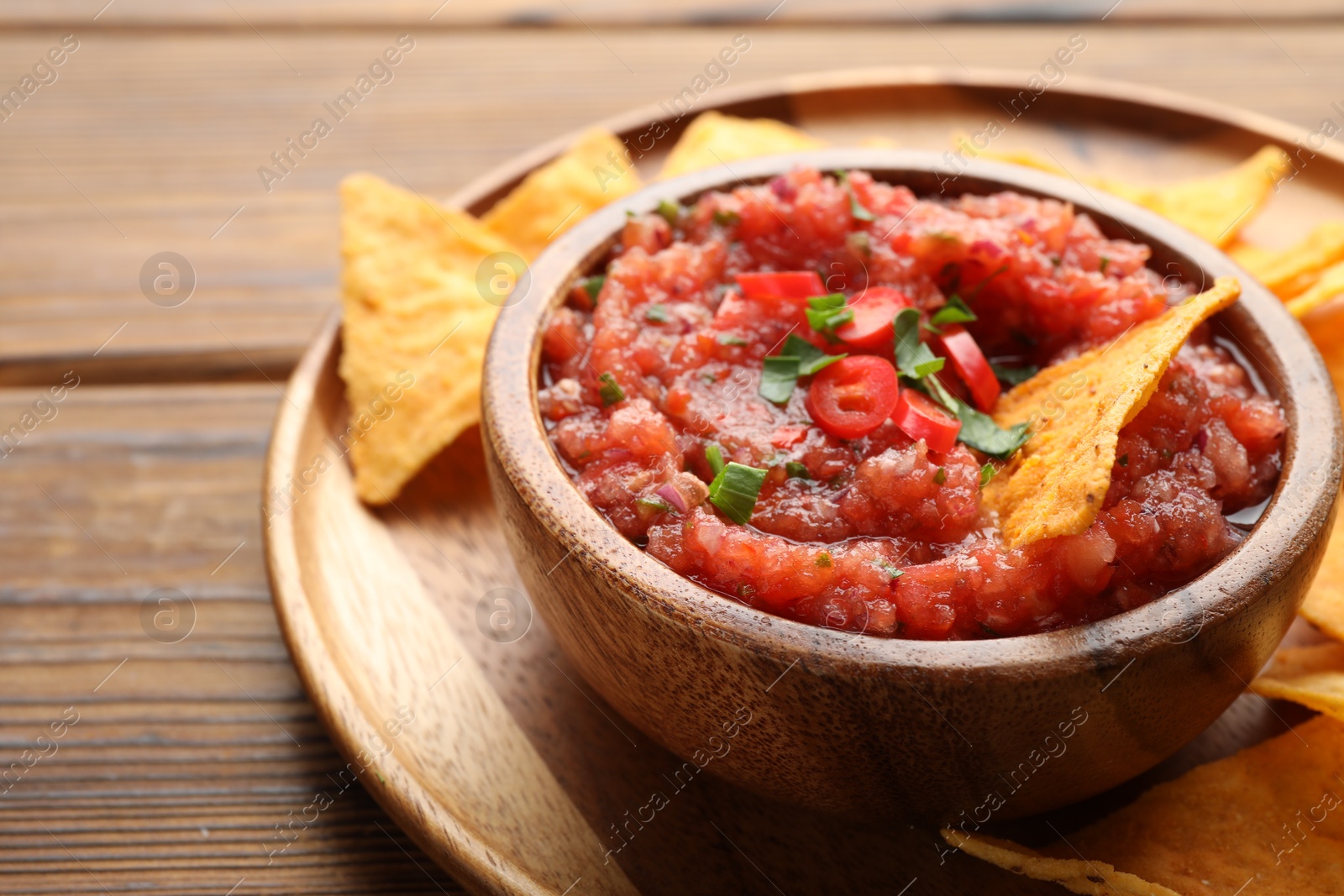 Photo of Delicious spicy salsa sauce in bowl and nacho chips on wooden table, closeup