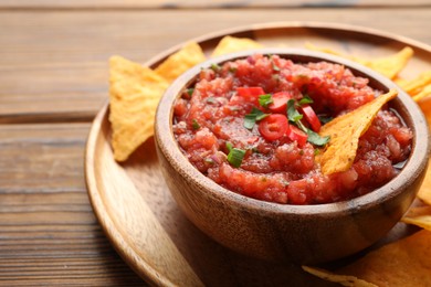 Photo of Delicious spicy salsa sauce in bowl and nacho chips on wooden table, closeup