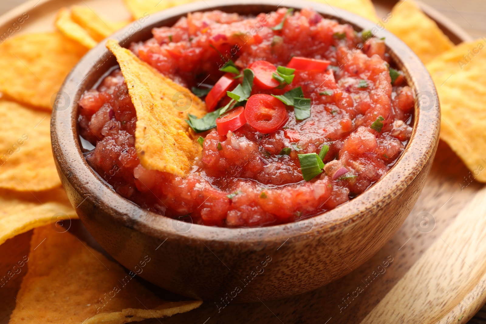 Photo of Delicious spicy salsa sauce in bowl and nacho chips on table, closeup