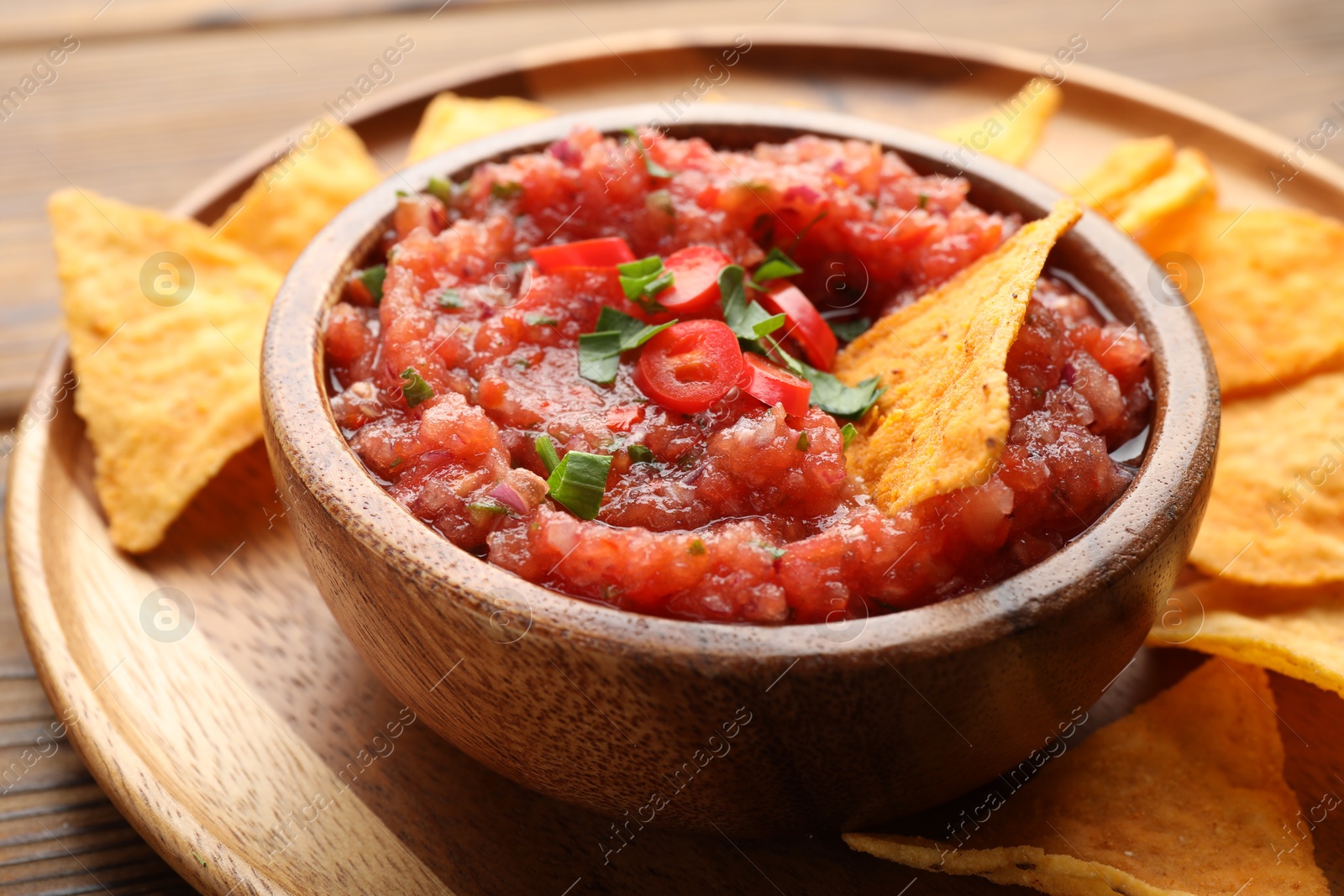 Photo of Delicious spicy salsa sauce in bowl and nacho chips on wooden table, closeup