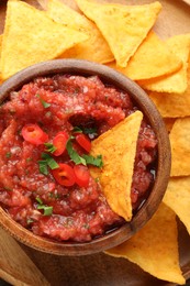 Delicious spicy salsa sauce in bowl and nacho chips on table, top view