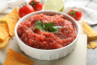 Delicious spicy salsa sauce in bowl and nacho chips on grey table, closeup