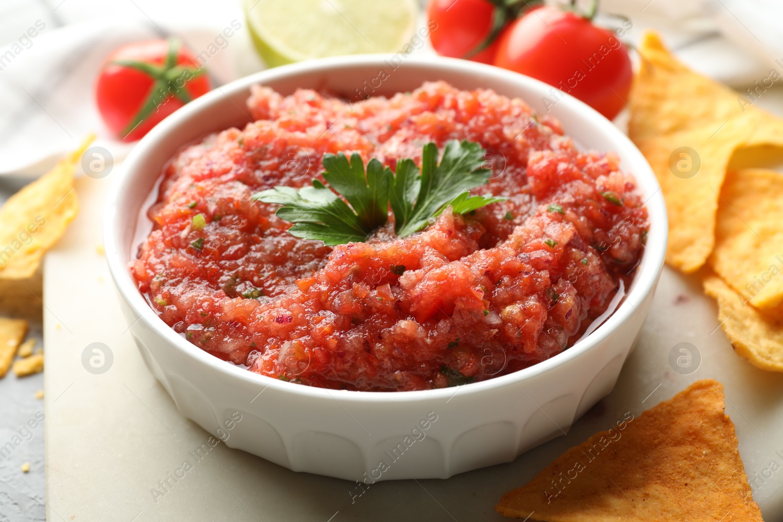 Photo of Delicious spicy salsa sauce in bowl and nacho chips on table, closeup