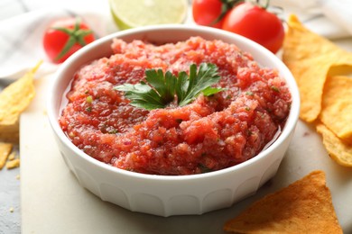 Photo of Delicious spicy salsa sauce in bowl and nacho chips on table, closeup