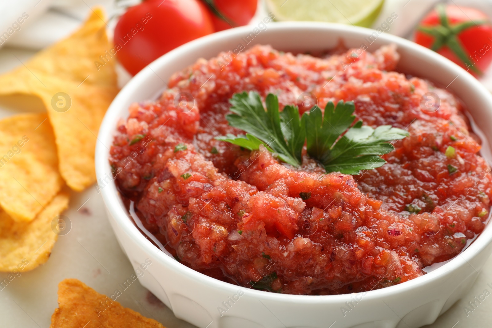 Photo of Delicious spicy salsa sauce in bowl and nacho chips on table, closeup