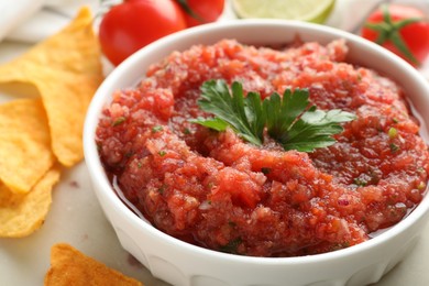 Photo of Delicious spicy salsa sauce in bowl and nacho chips on table, closeup