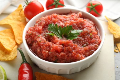 Delicious spicy salsa sauce in bowl and products on grey table, closeup