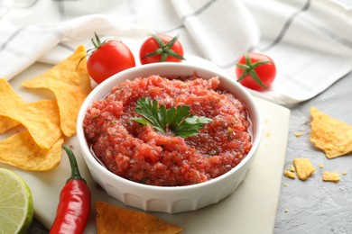 Photo of Delicious spicy salsa sauce in bowl and products on grey textured table, closeup