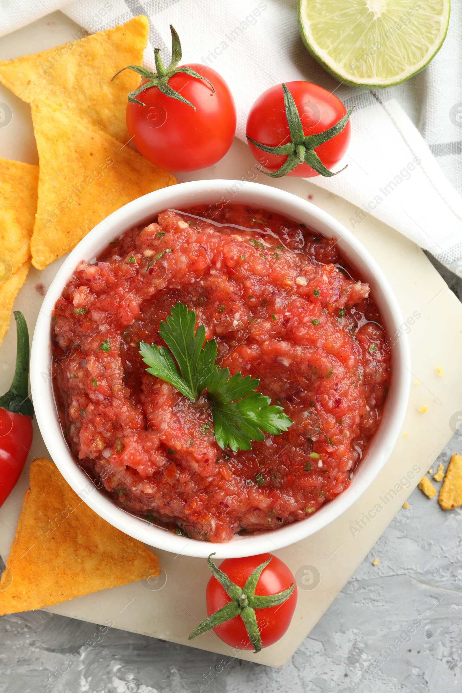 Photo of Delicious spicy salsa sauce in bowl and products on grey textured table, flat lay