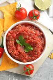 Photo of Delicious spicy salsa sauce in bowl and products on grey textured table, flat lay