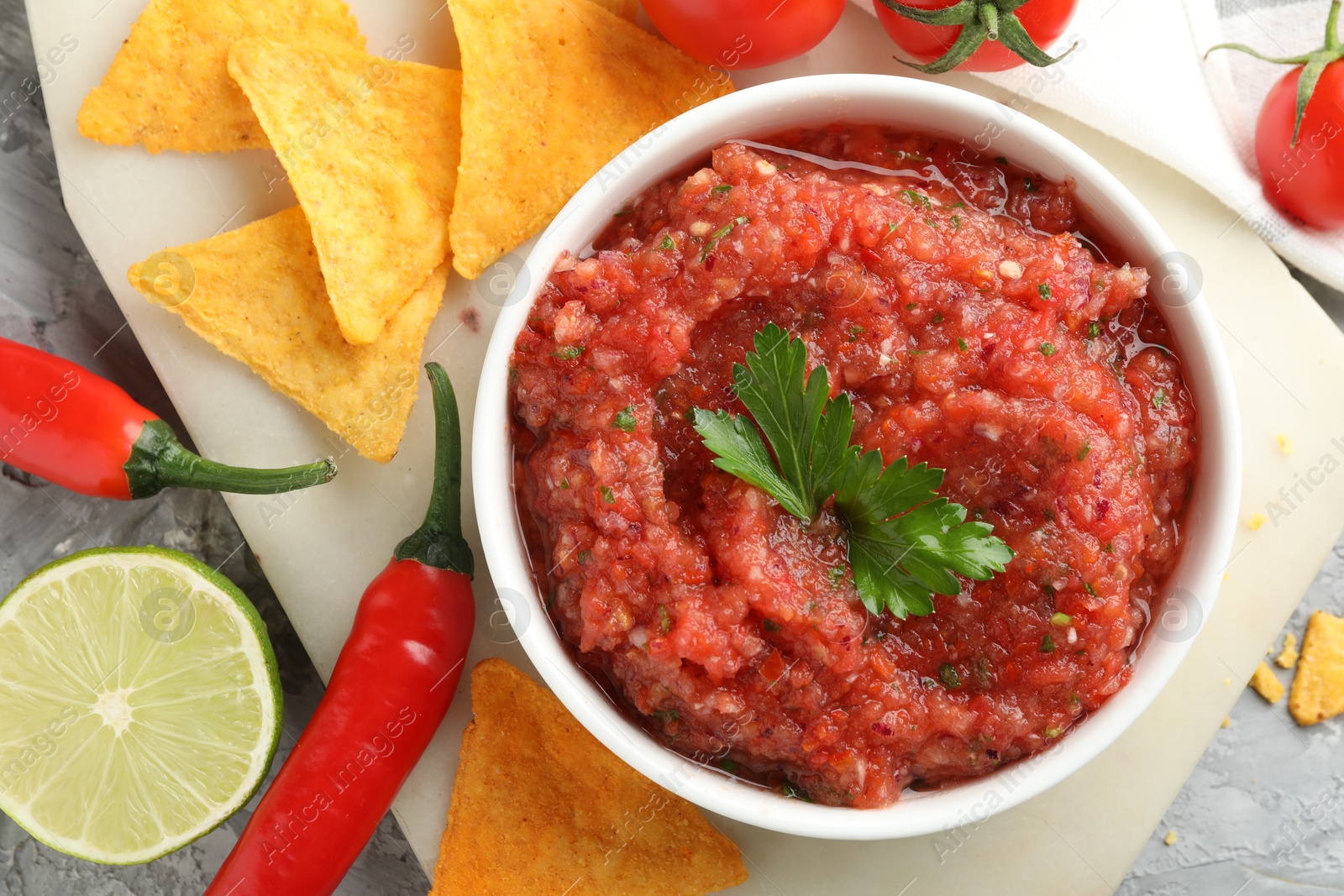 Photo of Delicious spicy salsa sauce in bowl and products on grey textured table, flat lay