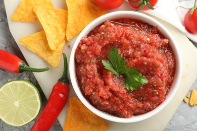 Delicious spicy salsa sauce in bowl and products on grey textured table, flat lay