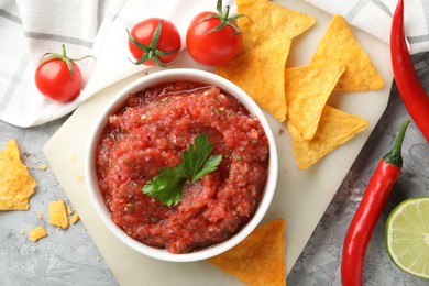 Delicious spicy salsa sauce in bowl and products on grey textured table, flat lay