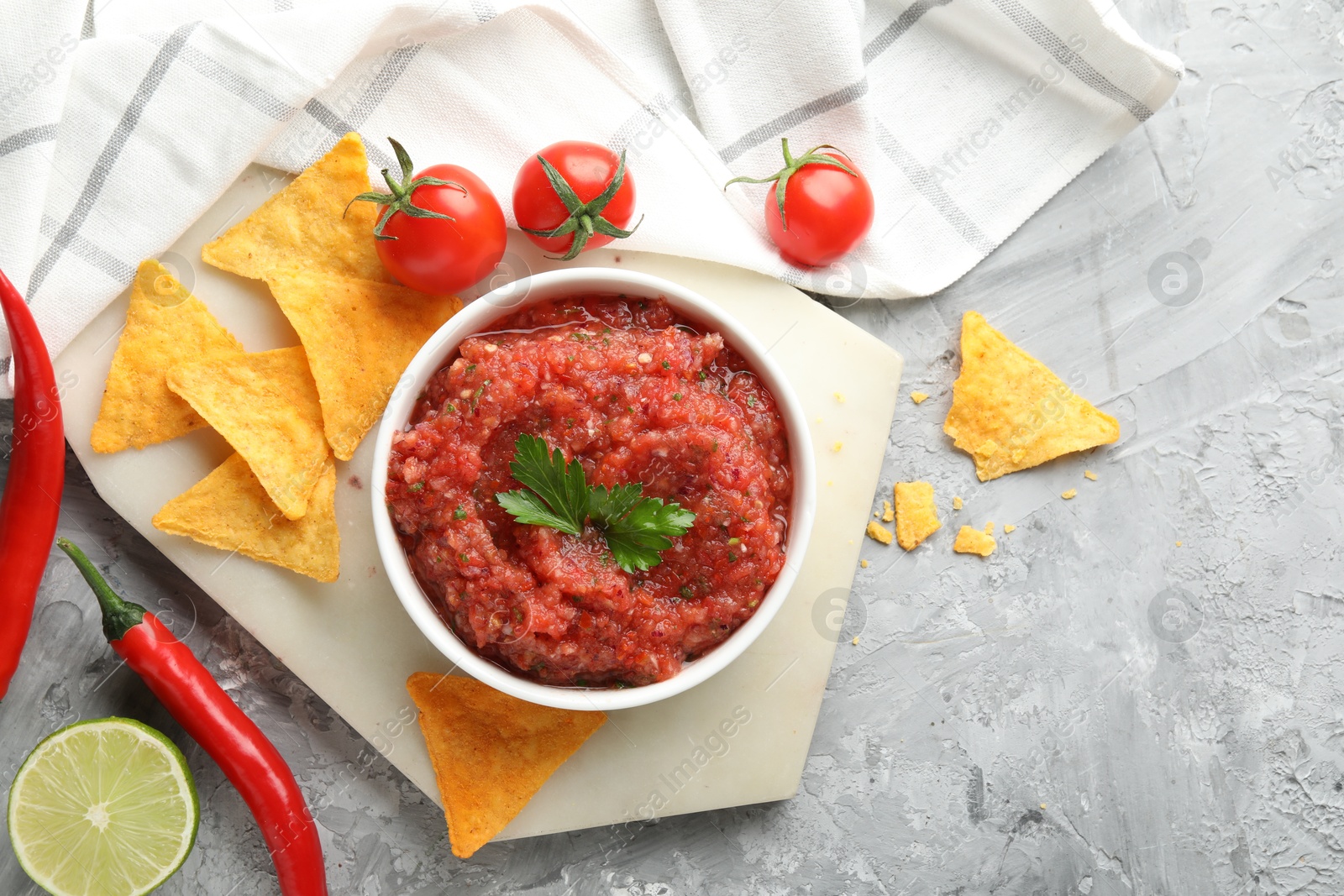 Photo of Delicious spicy salsa sauce in bowl and products on grey textured table, flat lay