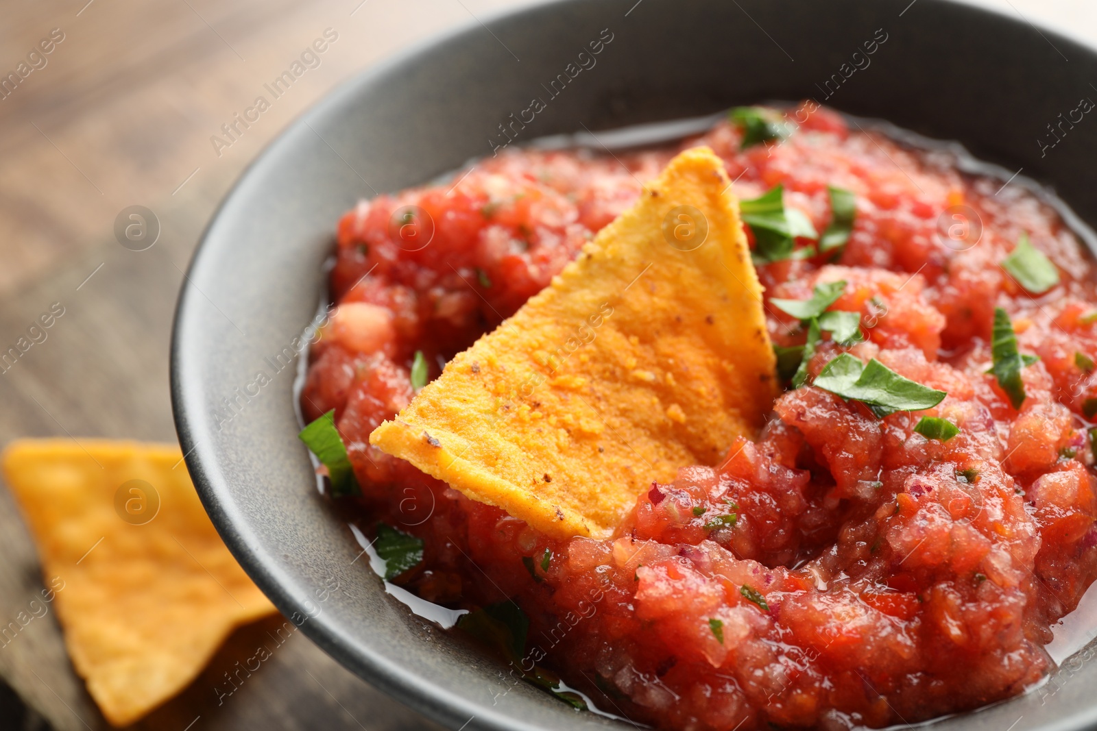 Photo of Delicious spicy salsa sauce with nacho chip in bowl on table, closeup