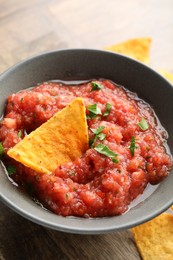 Delicious spicy salsa sauce with nacho chip in bowl on wooden table, closeup