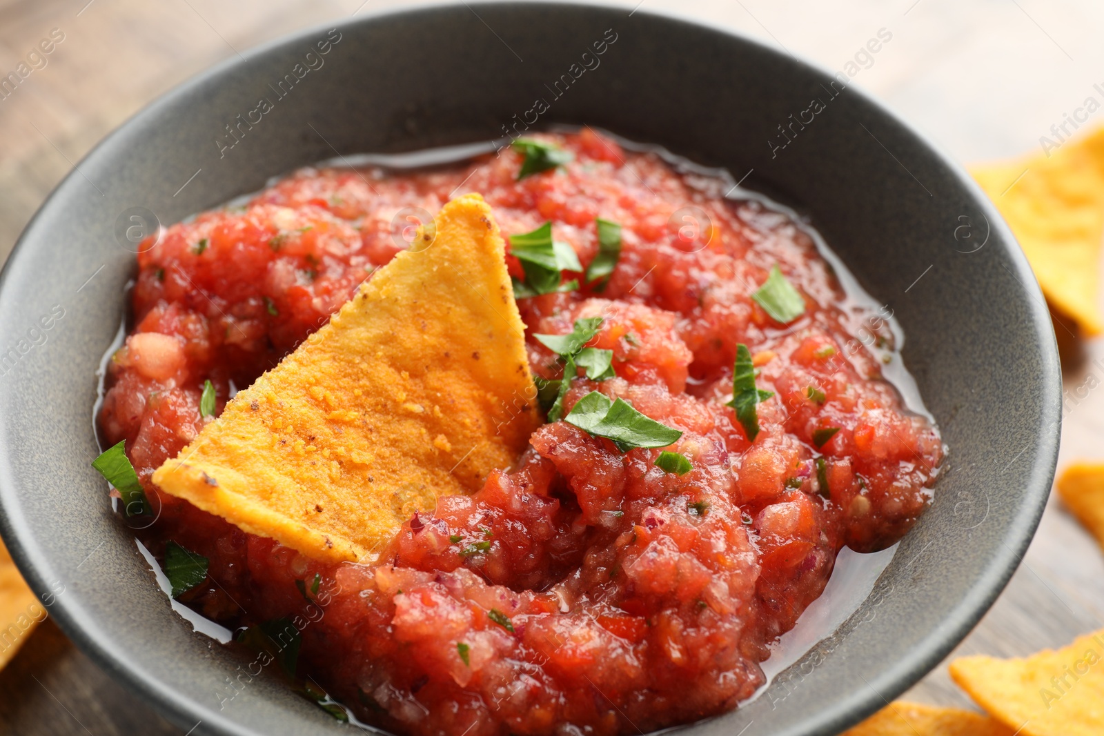 Photo of Delicious spicy salsa sauce with nacho chip in bowl on table, closeup