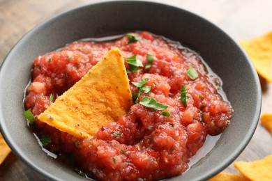 Delicious spicy salsa sauce with nacho chip in bowl on table, closeup