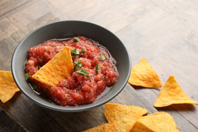 Photo of Delicious spicy salsa sauce in bowl and nacho chips on wooden table, closeup