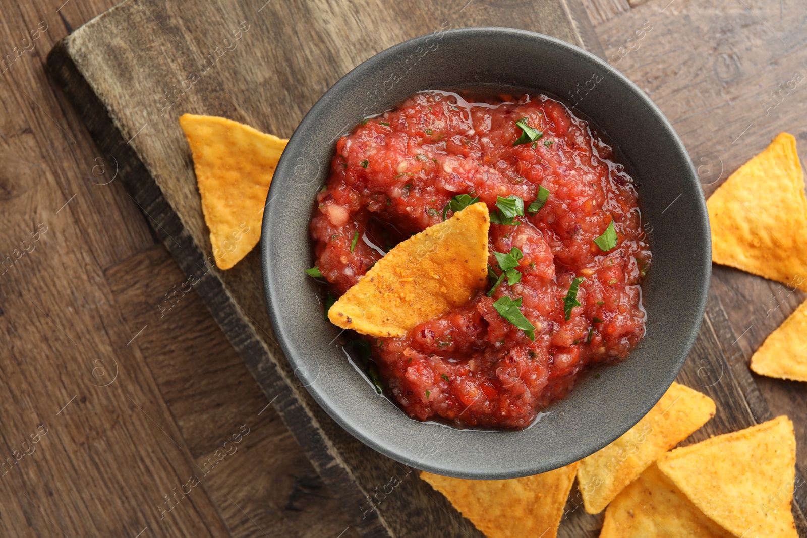 Photo of Delicious spicy salsa sauce in bowl and nacho chips on wooden table, top view