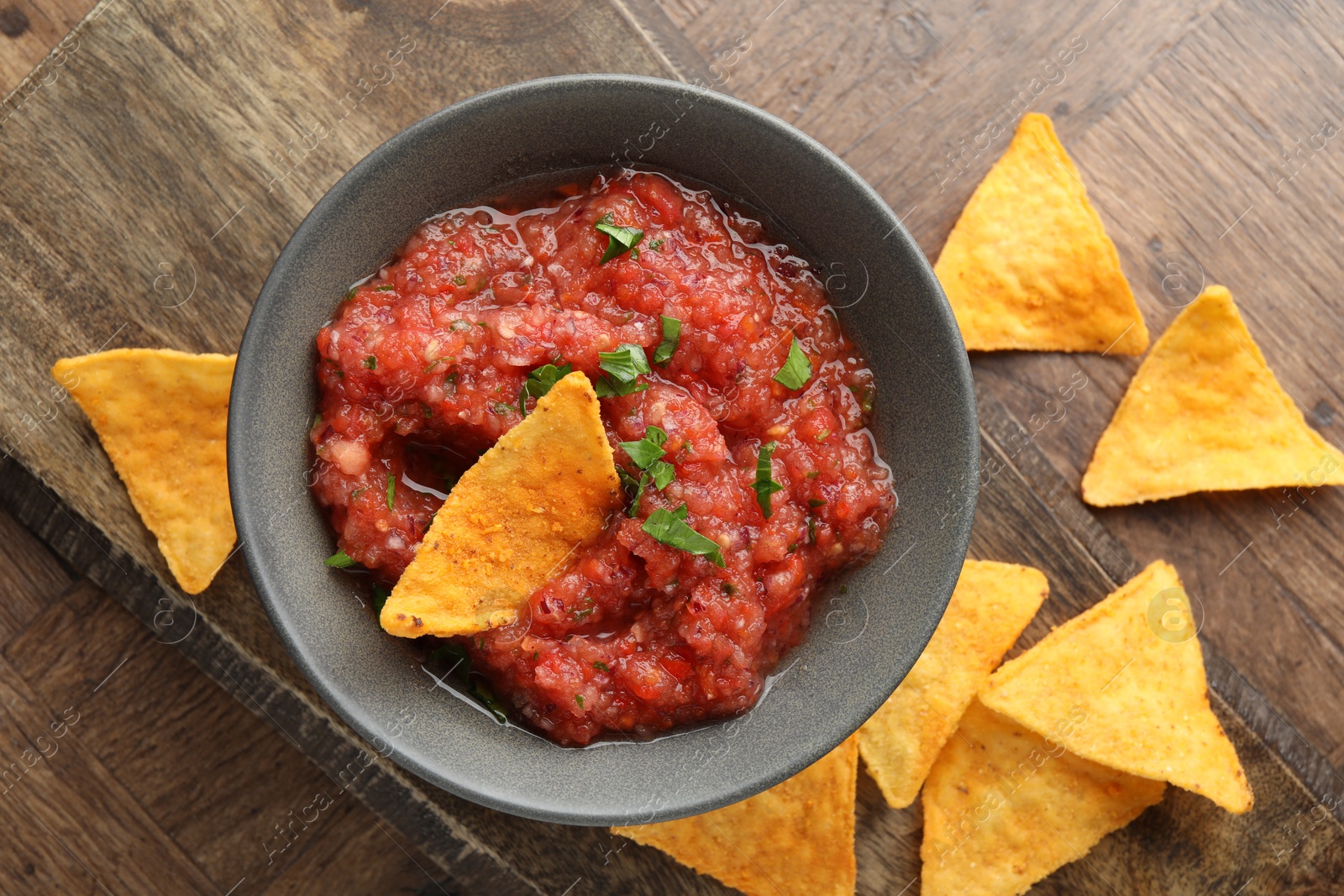 Photo of Delicious spicy salsa sauce in bowl and nacho chips on wooden table, top view