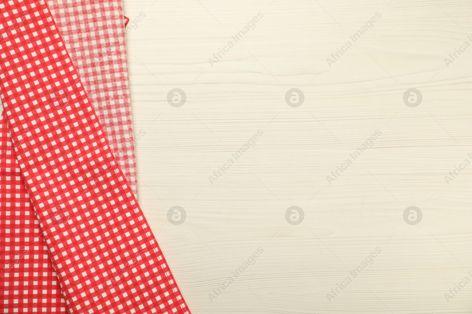 Photo of Red checkered tablecloth on white wooden background, top view. Space for text