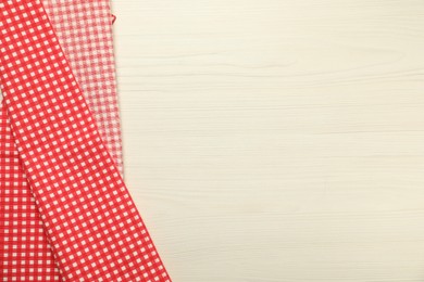 Photo of Red checkered tablecloth on white wooden background, top view. Space for text