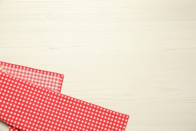 Photo of Red checkered tablecloth on white wooden background, top view. Space for text