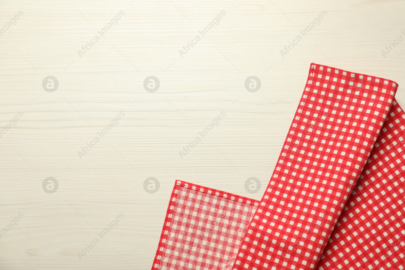 Photo of Red checkered tablecloth on white wooden background, top view. Space for text