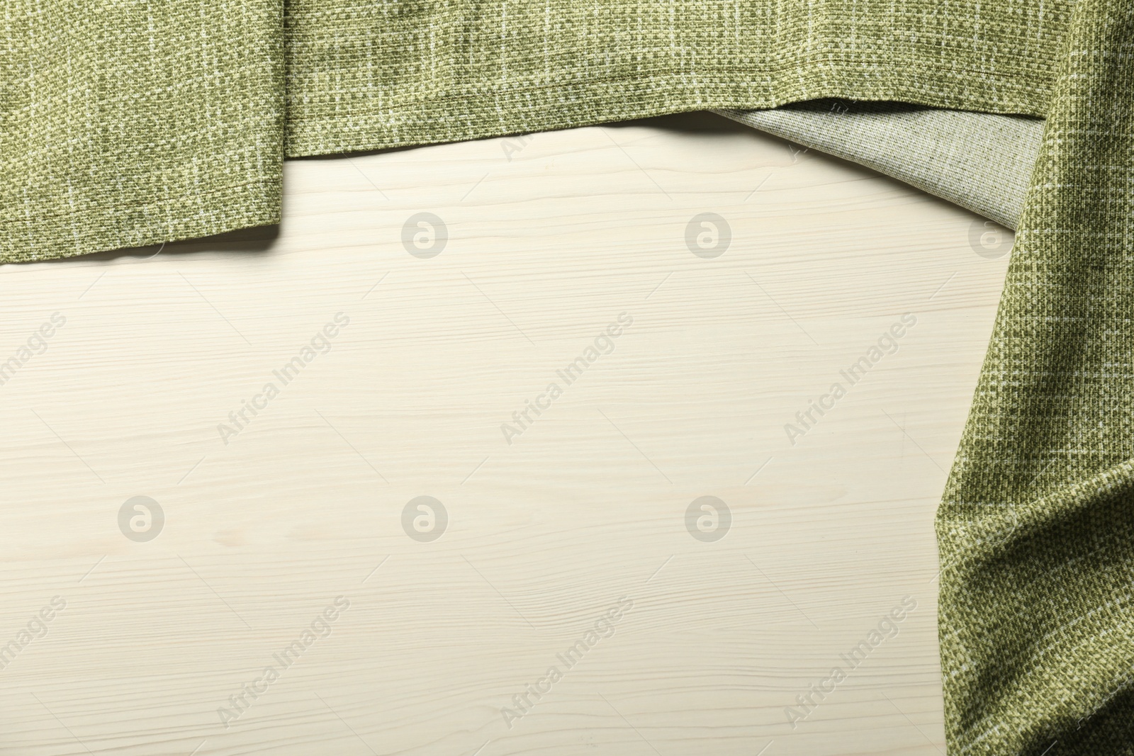 Photo of Green tablecloth on white wooden background, top view. Space for text