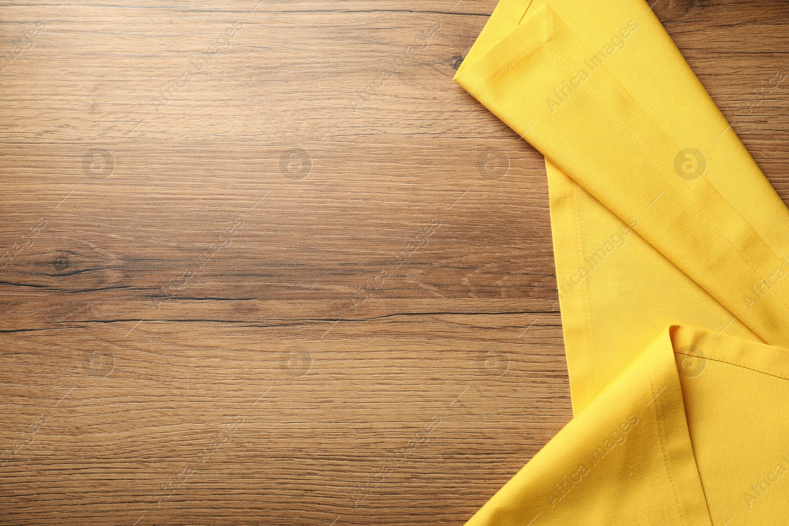 Photo of Yellow tablecloth on wooden background, top view. Space for text