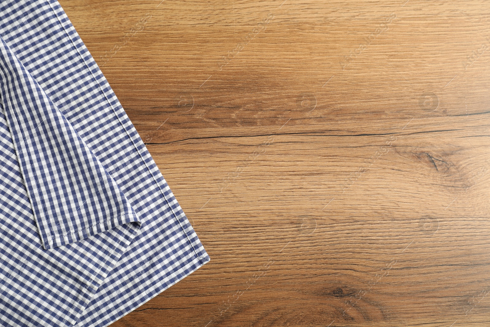 Photo of Checkered tablecloth on wooden background, top view. Space for text