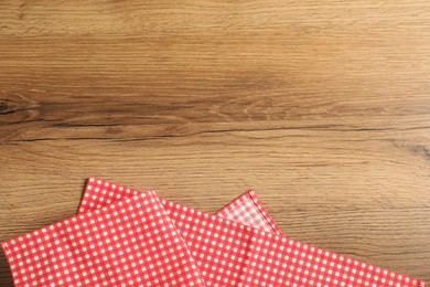 Photo of Red checkered tablecloth on wooden background, top view. Space for text