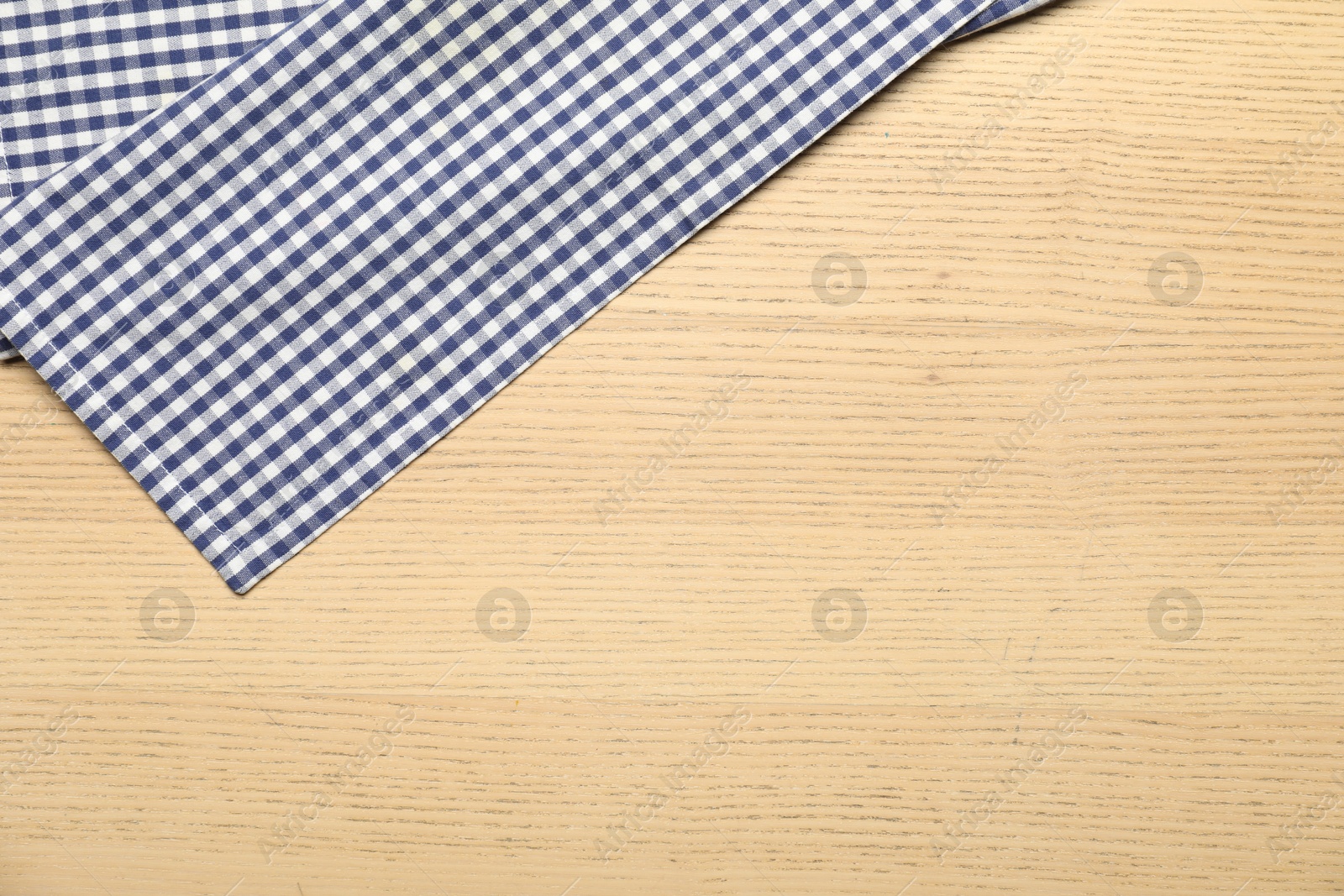 Photo of Checkered tablecloth on wooden background, top view. Space for text