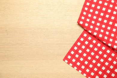 Photo of Red checkered tablecloth on wooden background, top view. Space for text