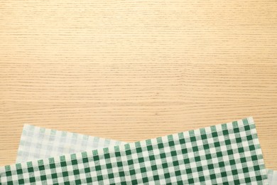 Photo of Green checkered tablecloth on wooden background, top view. Space for text