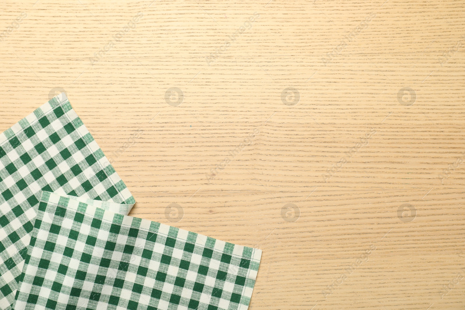 Photo of Green checkered tablecloth on wooden background, top view. Space for text