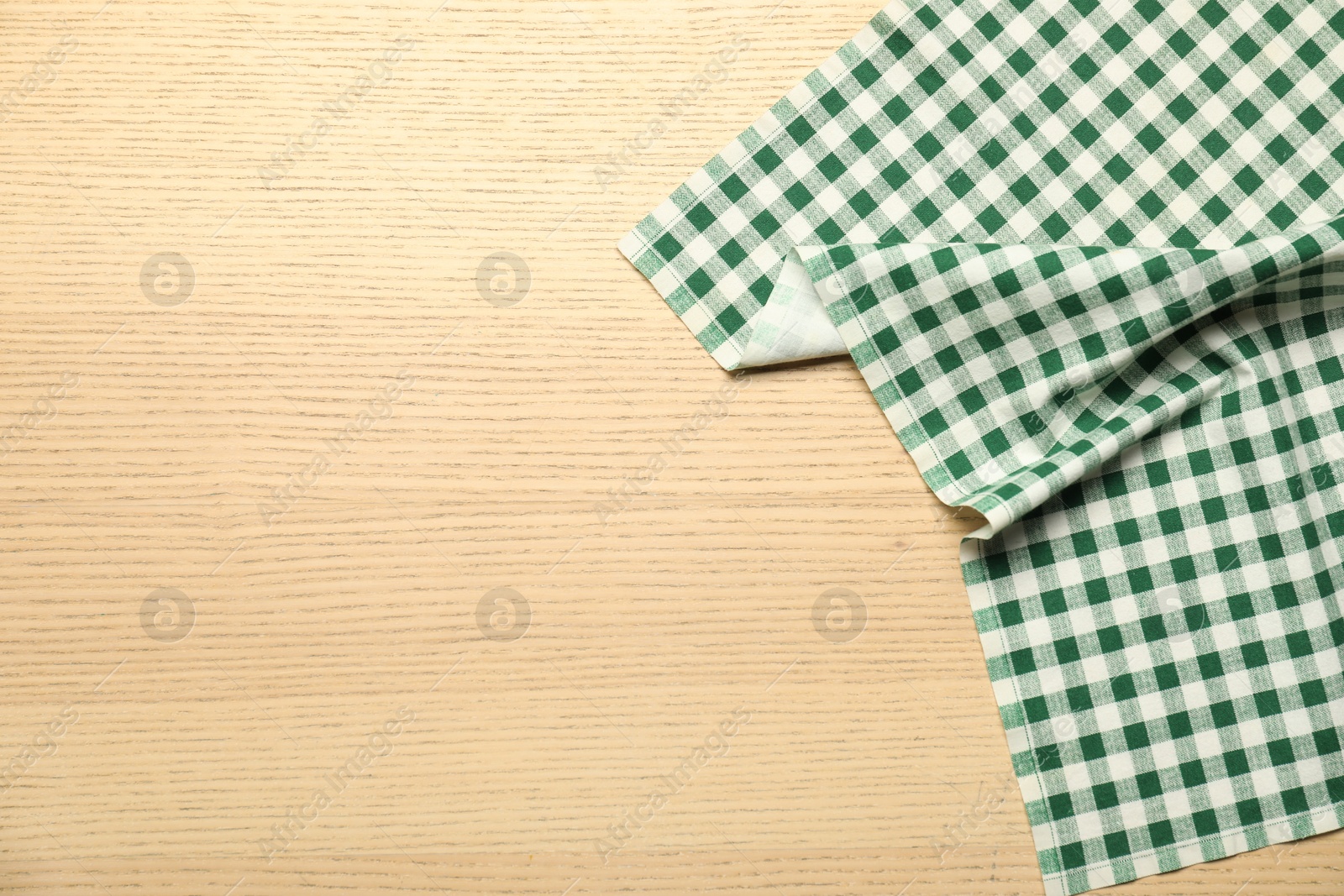 Photo of Green checkered tablecloth on wooden background, top view. Space for text