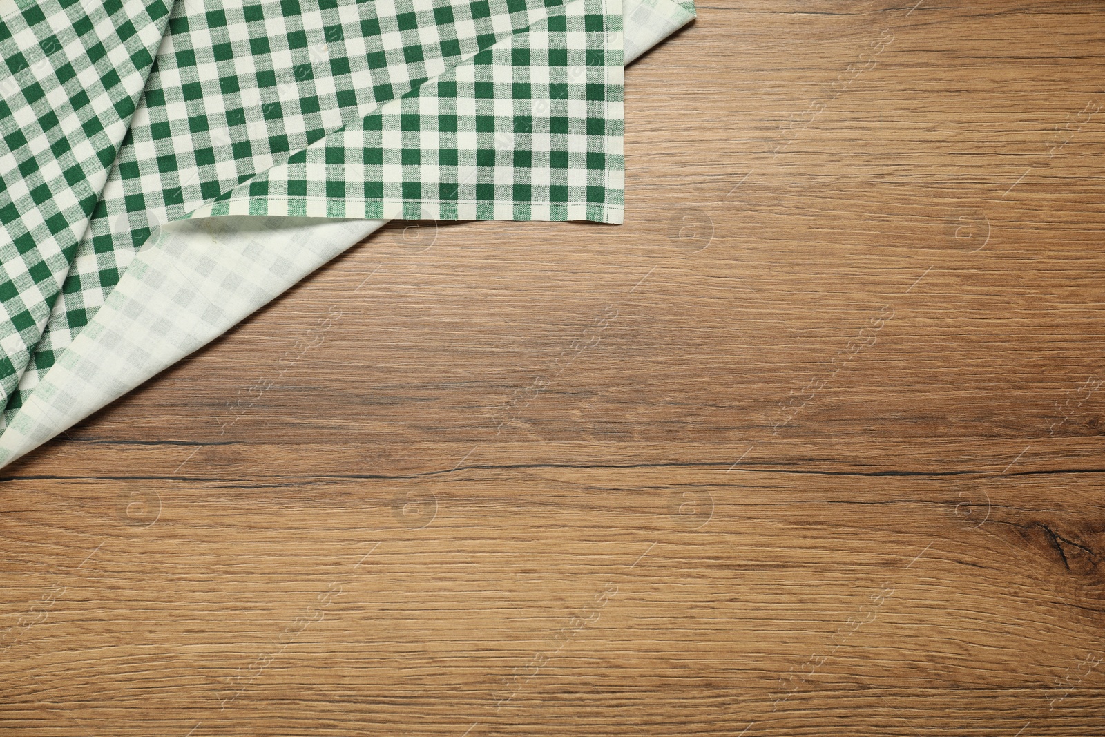 Photo of Green checkered tablecloth on wooden background, top view. Space for text