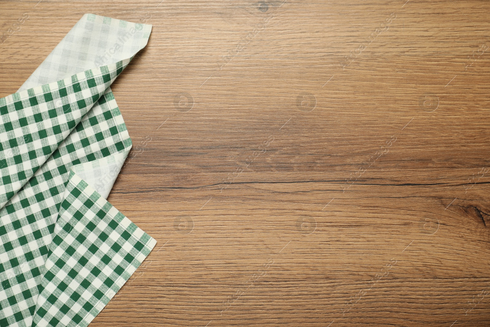 Photo of Green checkered tablecloth on wooden background, top view. Space for text