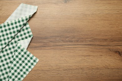 Photo of Green checkered tablecloth on wooden background, top view. Space for text