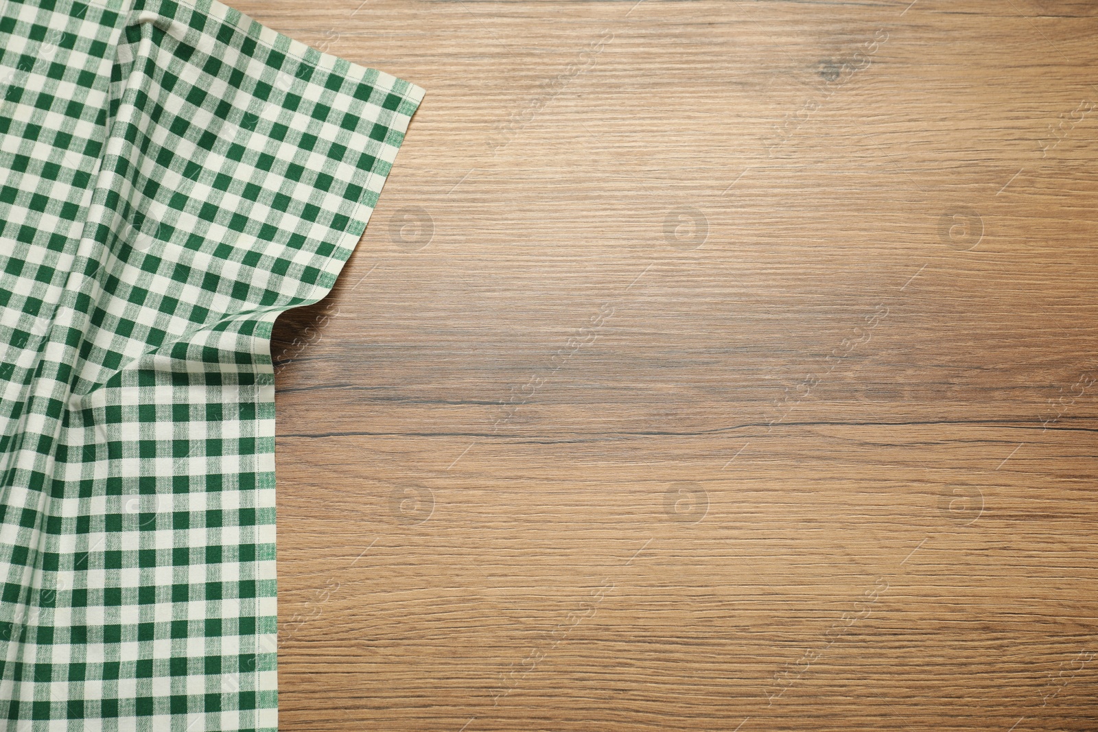 Photo of Green checkered tablecloth on wooden background, top view. Space for text