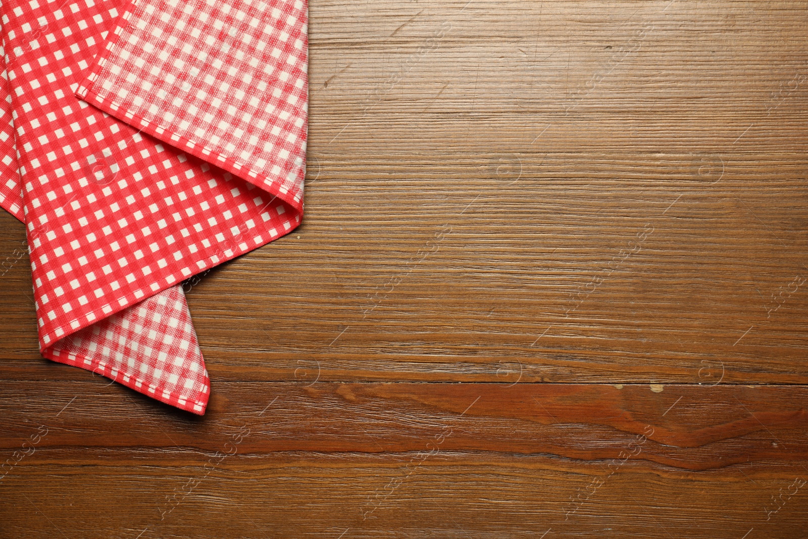 Photo of Red checkered tablecloth on wooden background, top view. Space for text